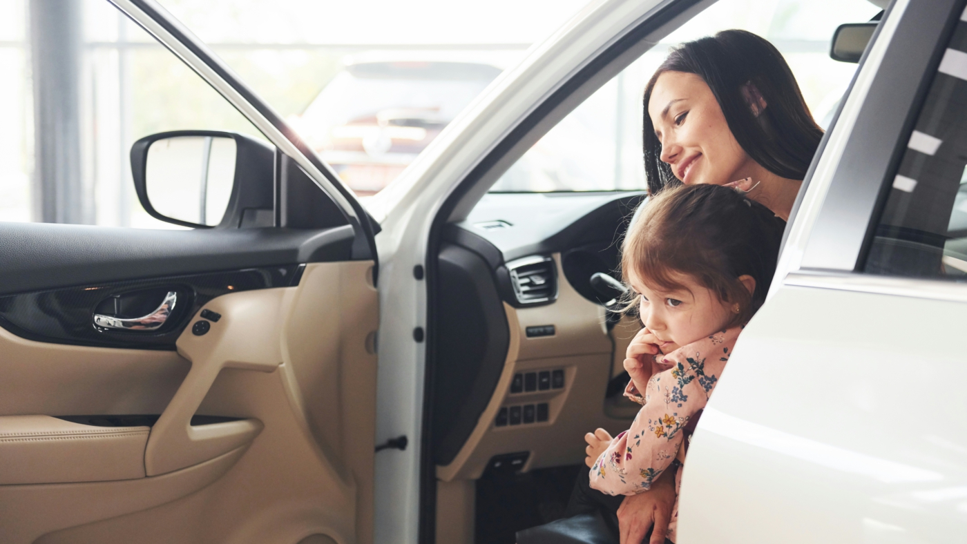 Mann im Anzug mit Klemmbrett inspiziert ein Auto in einem Autohaus.