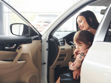Mann im Anzug mit Klemmbrett inspiziert ein Auto in einem Autohaus.
