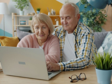 Älteres Paar sitzt gemeinsam vor einem Laptop am Wohnzimmertisch