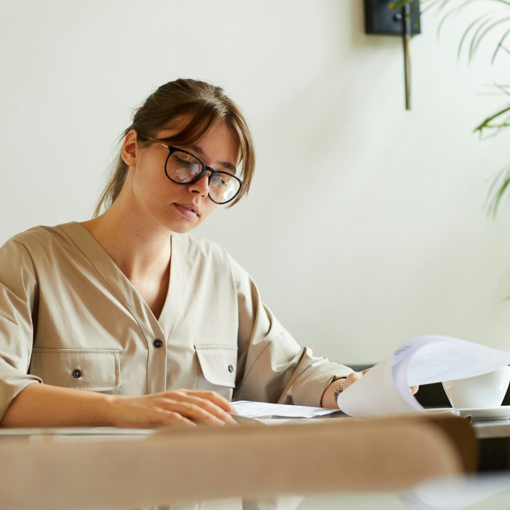 Frau mit Brille prüft Dokumente am Tisch.