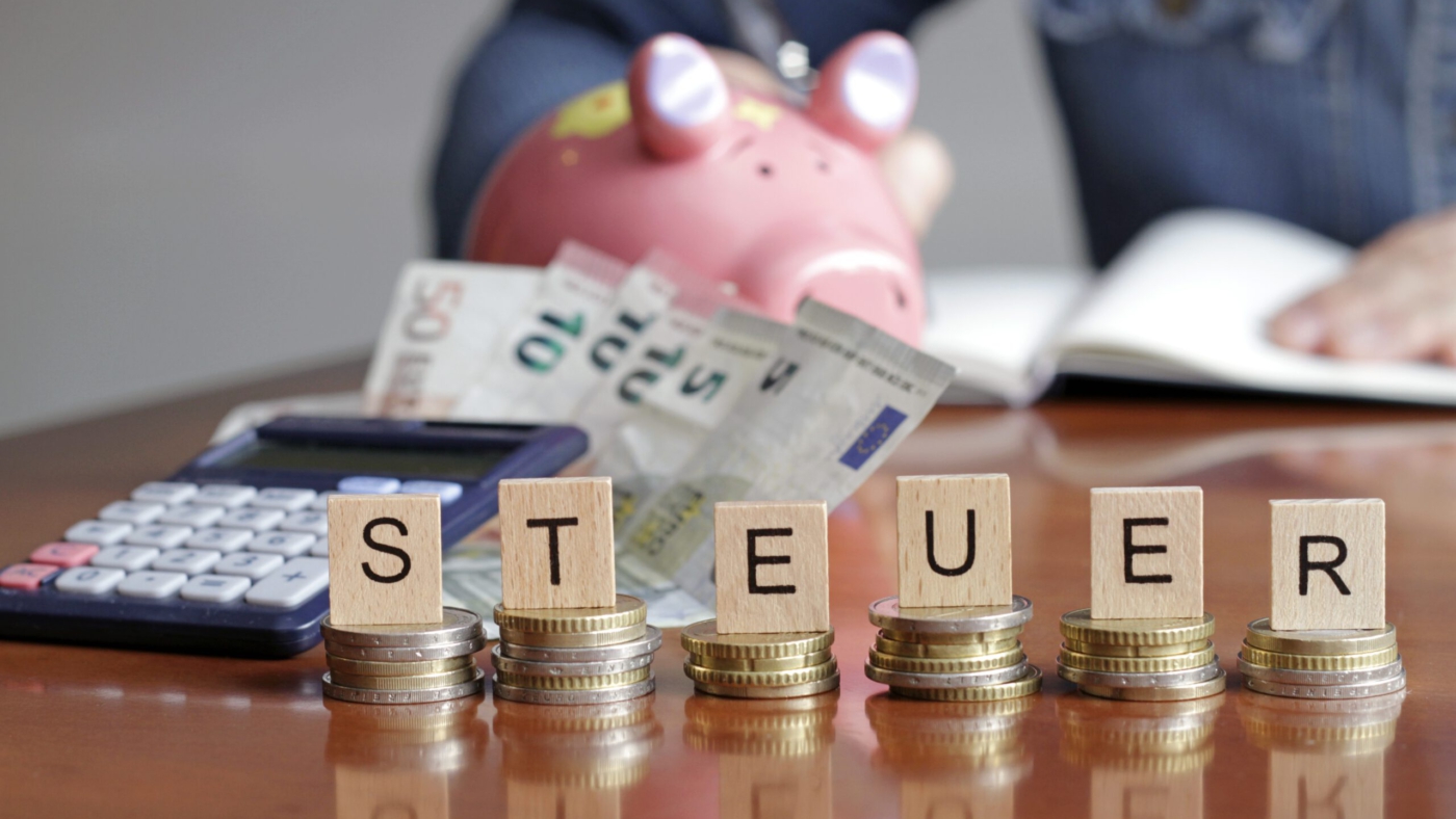 Münzstapel mit Holzbuchstaben bilden das Wort Steuer.