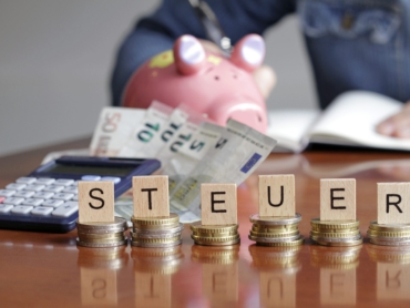 Münzstapel mit Holzbuchstaben bilden das Wort Steuer.