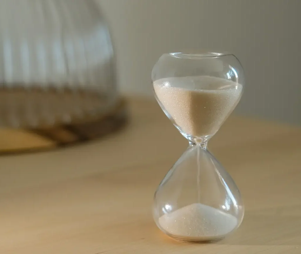 Glas-Sanduhr mit rieselndem Sand auf einem Tisch im weichen Licht