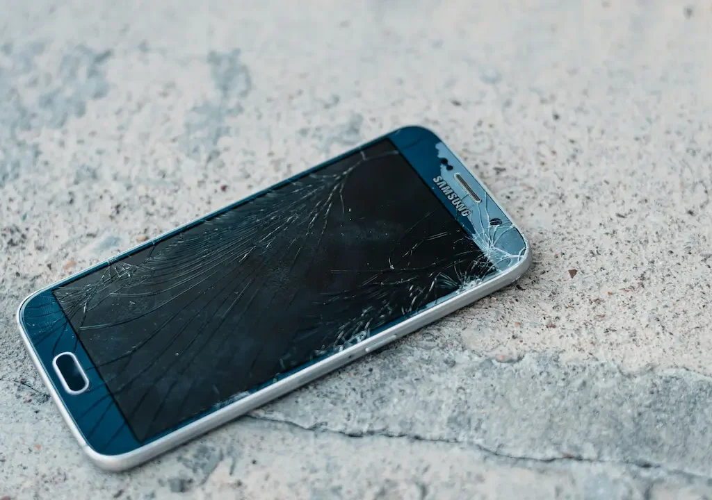 Smartphone mit stark gesprungenem Display liegt auf rauem Untergrund